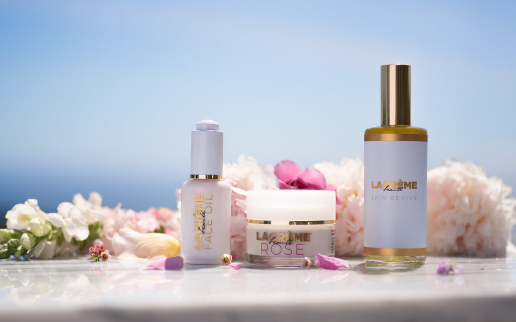 rose face oil, rose cream and skin revive face mist against a bright blue sky, surrounded by white and pink flowers and petals