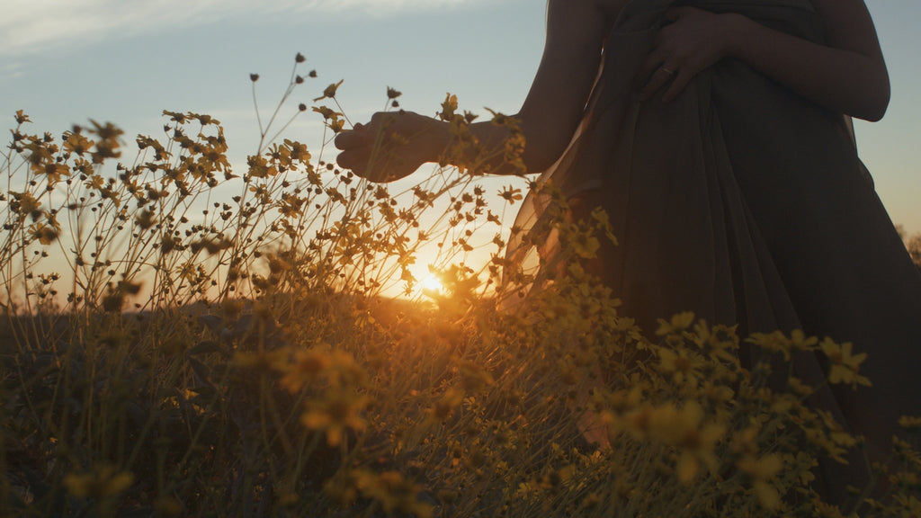 woman walking at sunset, running her hands through yellow wild flowers